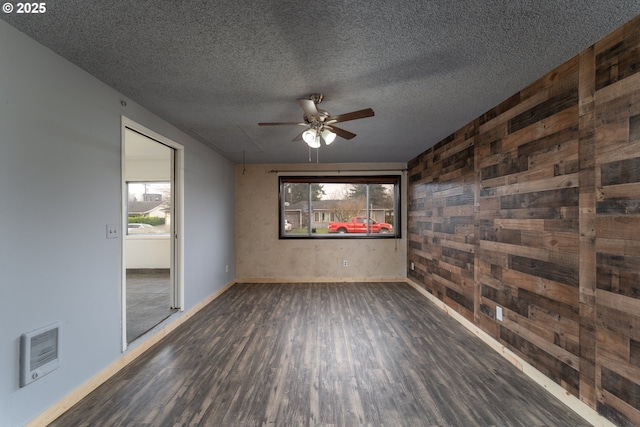 spare room featuring wood walls, ceiling fan, dark wood-type flooring, and a textured ceiling