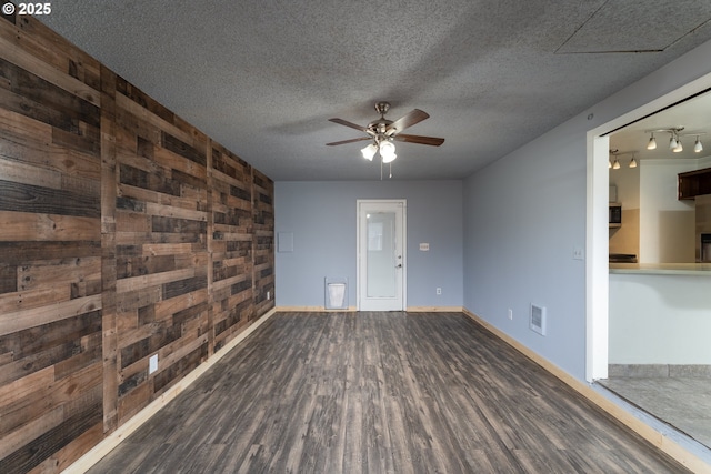 empty room with ceiling fan, dark hardwood / wood-style flooring, wood walls, track lighting, and a textured ceiling