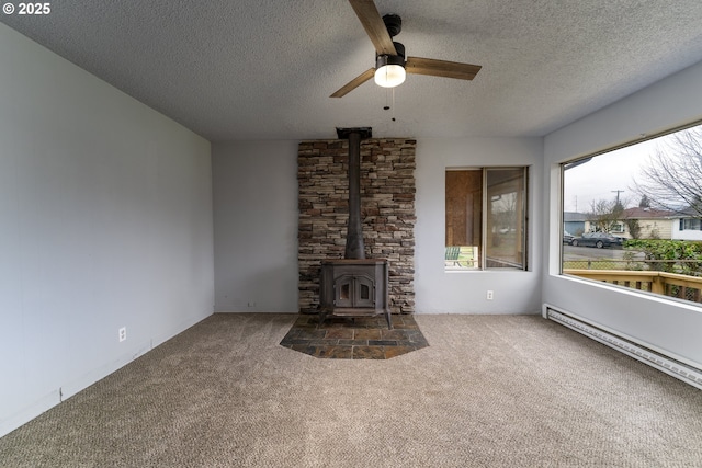 unfurnished living room featuring a wood stove, ceiling fan, baseboard heating, a textured ceiling, and dark carpet