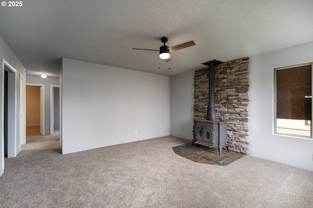 unfurnished living room featuring carpet, a textured ceiling, a wood stove, and ceiling fan