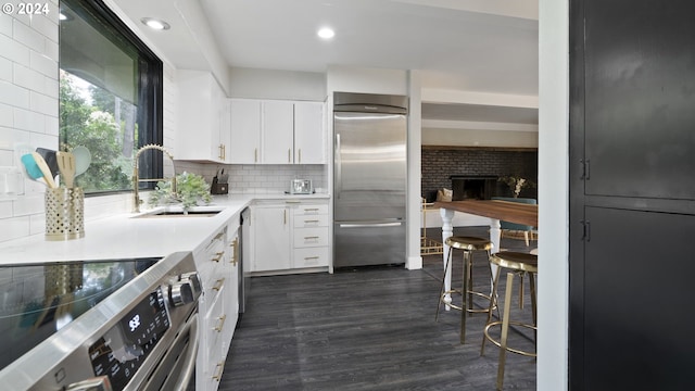 kitchen featuring dark wood-style floors, appliances with stainless steel finishes, backsplash, white cabinetry, and a sink