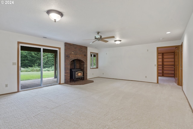 unfurnished living room with light colored carpet, ceiling fan, and a wood stove