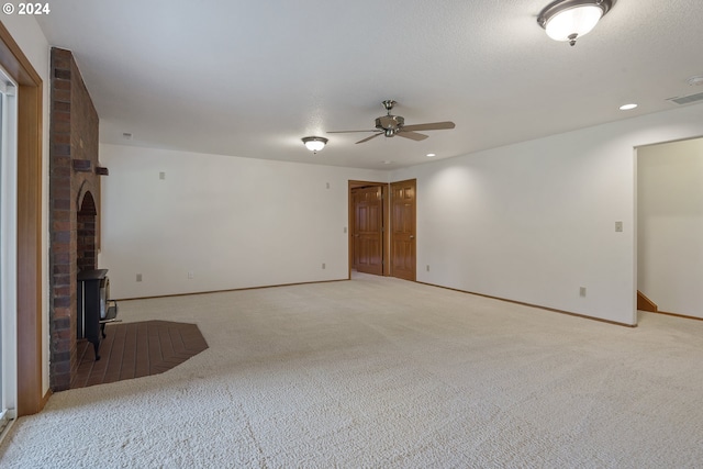 carpeted spare room featuring brick wall, ceiling fan, and a wood stove