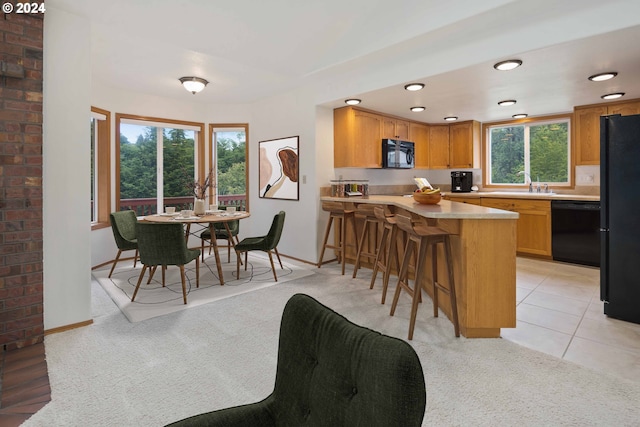 kitchen featuring light carpet, a breakfast bar, black appliances, and sink