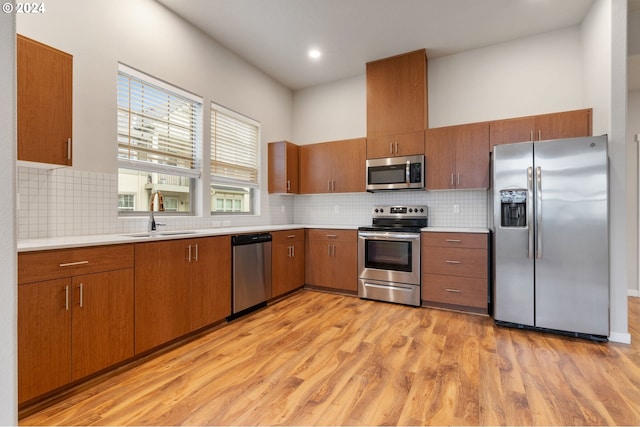 kitchen with decorative backsplash, light wood-type flooring, stainless steel appliances, and sink