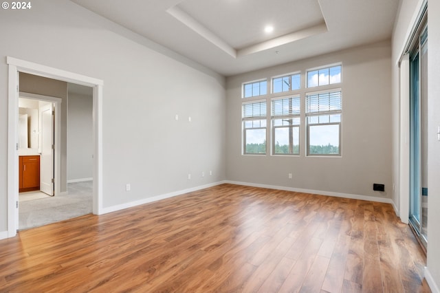 unfurnished bedroom featuring a raised ceiling, light hardwood / wood-style flooring, and ensuite bath