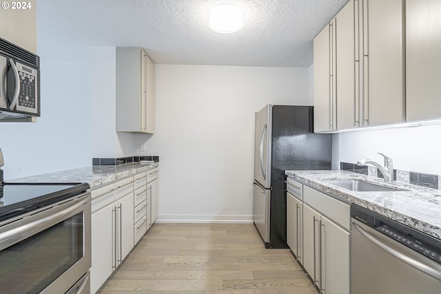 kitchen featuring light stone countertops, a textured ceiling, stainless steel appliances, sink, and light hardwood / wood-style floors