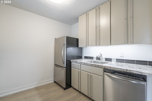 kitchen featuring sink, light stone countertops, a textured ceiling, light wood-type flooring, and stainless steel appliances