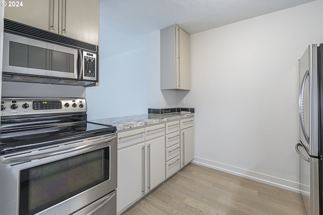 kitchen featuring light hardwood / wood-style floors, light stone counters, a textured ceiling, and appliances with stainless steel finishes