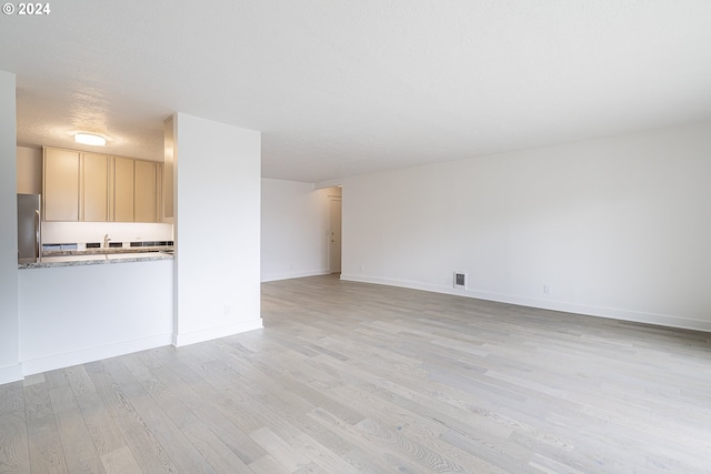 unfurnished living room with a textured ceiling, light hardwood / wood-style floors, and sink