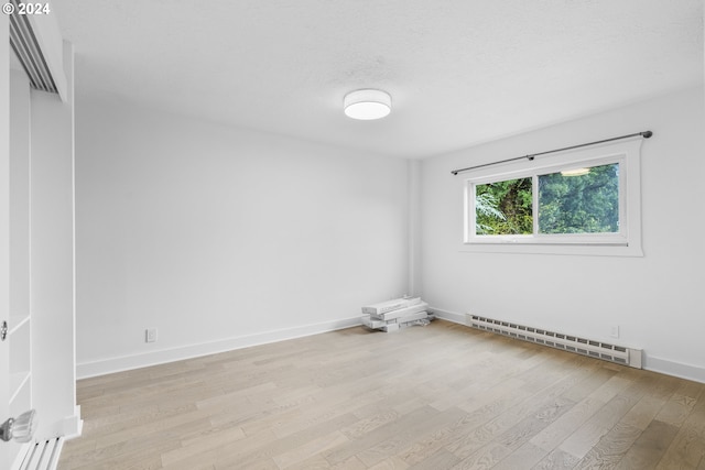 spare room featuring baseboard heating and light hardwood / wood-style flooring