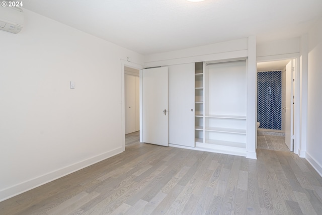 unfurnished bedroom with light wood-type flooring, a wall mounted AC, and a closet