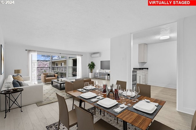 dining area featuring a wall mounted air conditioner, light hardwood / wood-style floors, and a textured ceiling