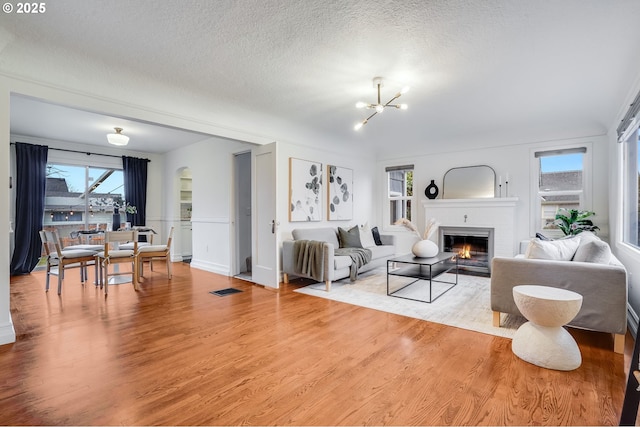 living room featuring wood-type flooring, a textured ceiling, an inviting chandelier, and a fireplace