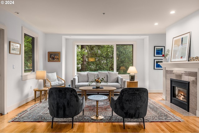 living room with baseboards, light wood-style floors, a tile fireplace, and a healthy amount of sunlight