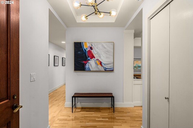 hallway featuring a tray ceiling, light hardwood / wood-style floors, and an inviting chandelier