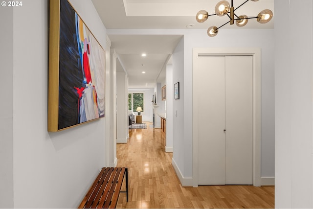 corridor featuring light wood-style floors, baseboards, a notable chandelier, and recessed lighting