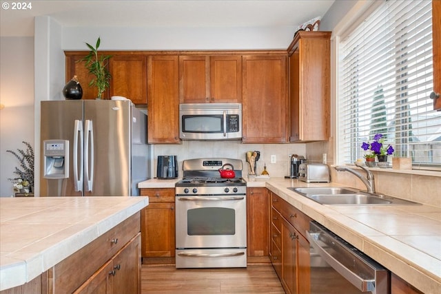 kitchen with appliances with stainless steel finishes, tile counters, sink, and light hardwood / wood-style floors