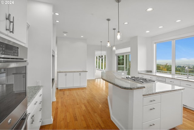 kitchen featuring stainless steel appliances, decorative light fixtures, light wood-type flooring, and white cabinets