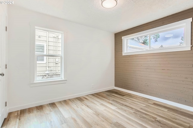 spare room with a textured ceiling, light hardwood / wood-style flooring, and wooden walls