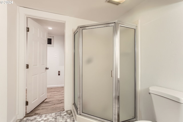 bathroom with hardwood / wood-style floors, toilet, and a shower with door