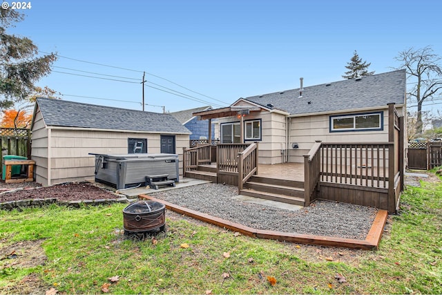 rear view of house with a hot tub, an outdoor fire pit, a lawn, and a wooden deck