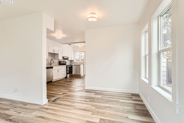 interior space with decorative backsplash, appliances with stainless steel finishes, light wood-type flooring, sink, and white cabinets