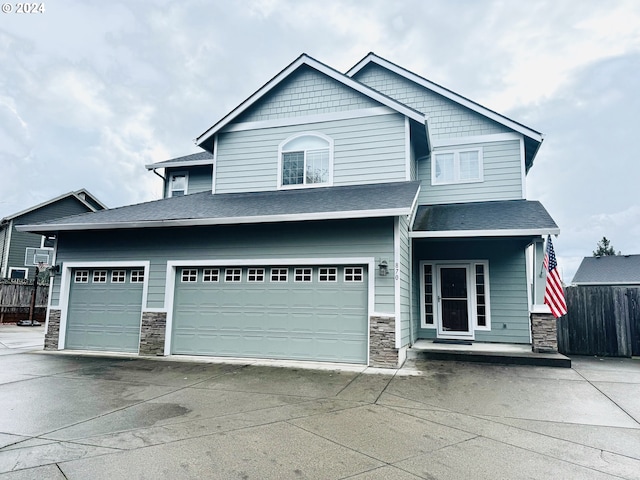 craftsman-style home with stone siding, fence, driveway, covered porch, and an attached garage