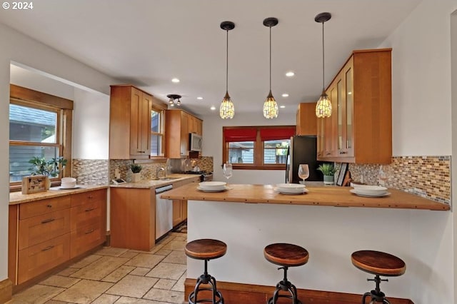 kitchen with pendant lighting, stainless steel appliances, a kitchen breakfast bar, kitchen peninsula, and decorative backsplash