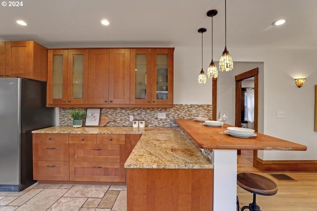 kitchen with stainless steel fridge, tasteful backsplash, hanging light fixtures, kitchen peninsula, and light stone counters