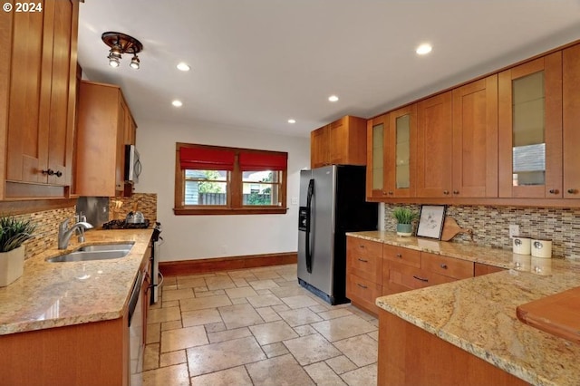 kitchen with tasteful backsplash, stainless steel appliances, light stone counters, and sink