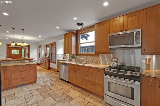 kitchen featuring pendant lighting, backsplash, stainless steel appliances, light stone counters, and sink