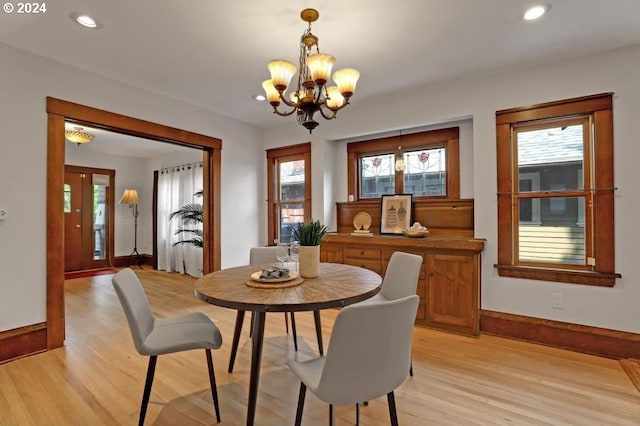 dining area with light wood-type flooring, a healthy amount of sunlight, and an inviting chandelier