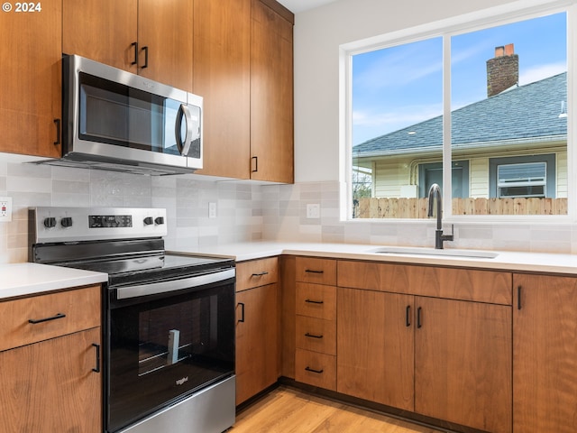 kitchen with tasteful backsplash, sink, stainless steel appliances, and light wood-type flooring