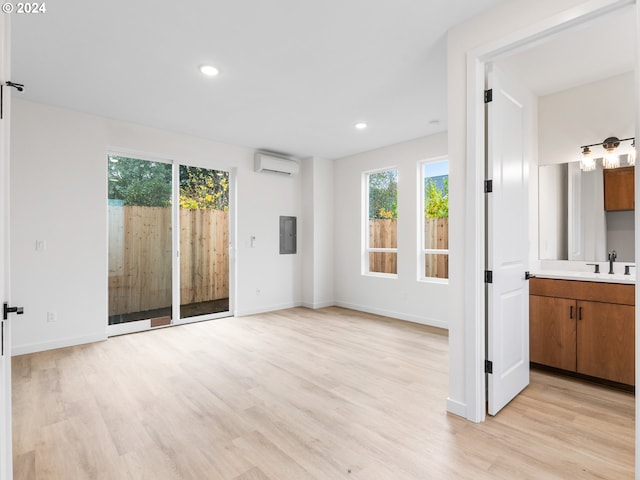 unfurnished living room featuring sink, a wall mounted AC, electric panel, and light wood-type flooring