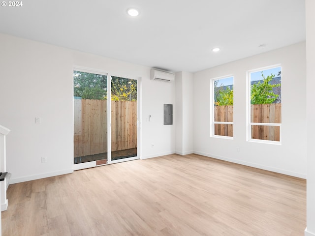 unfurnished living room with a wealth of natural light, electric panel, a wall unit AC, and light hardwood / wood-style flooring