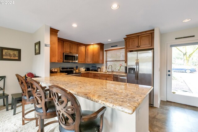 kitchen featuring kitchen peninsula, light tile flooring, appliances with stainless steel finishes, and a breakfast bar