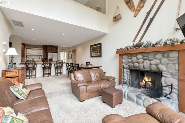 living room featuring a stone fireplace, a towering ceiling, and light colored carpet