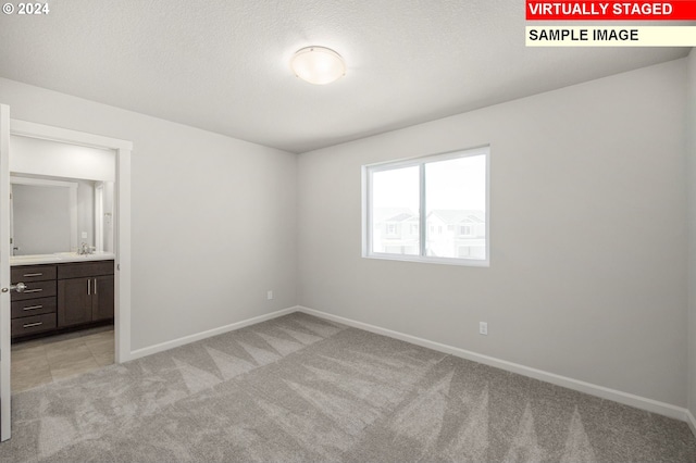 unfurnished bedroom featuring light carpet, a textured ceiling, connected bathroom, and sink