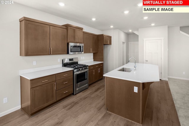 kitchen featuring light hardwood / wood-style floors, sink, stainless steel appliances, and an island with sink