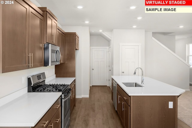 kitchen with sink, an island with sink, light hardwood / wood-style floors, and appliances with stainless steel finishes