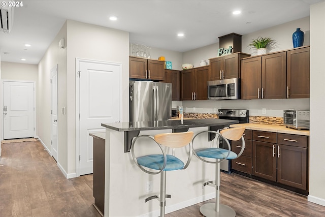 kitchen featuring appliances with stainless steel finishes, dark hardwood / wood-style flooring, a kitchen island, and a breakfast bar area