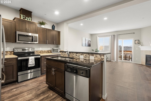 kitchen with a tile fireplace, sink, appliances with stainless steel finishes, dark hardwood / wood-style flooring, and dark brown cabinetry