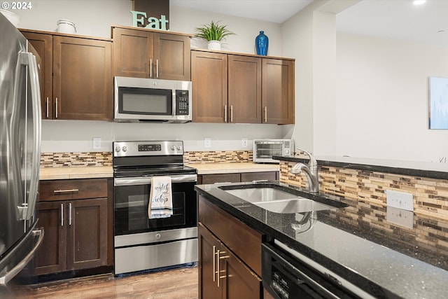 kitchen with appliances with stainless steel finishes, dark brown cabinets, sink, dark stone countertops, and light hardwood / wood-style floors