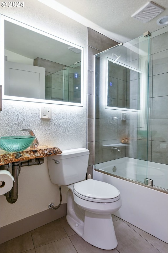 full bathroom with a textured ceiling, bath / shower combo with glass door, toilet, sink, and tile patterned floors