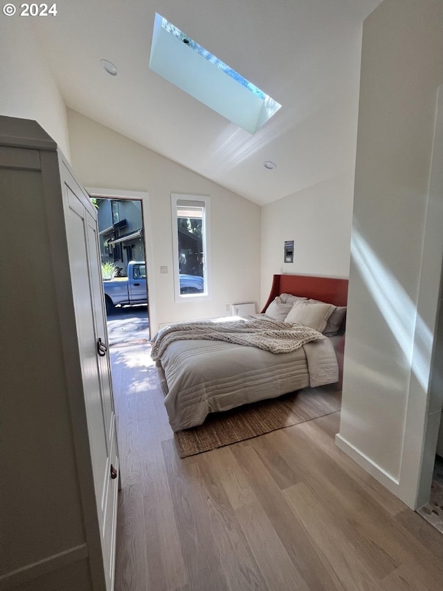 bedroom with vaulted ceiling with skylight and light hardwood / wood-style floors