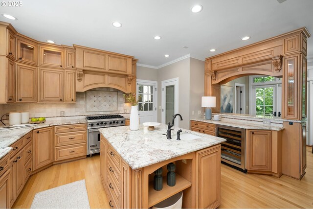 4243 SW Bertha Ave, Portland, OR 97239 - kitchen with designer range, beverage cooler, light wood finished floors, ornamental molding, and an island with sink