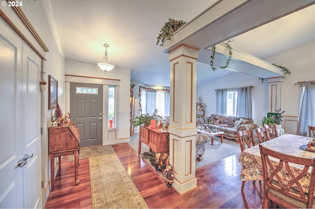 foyer with hardwood / wood-style floors, vaulted ceiling, plenty of natural light, and ornate columns