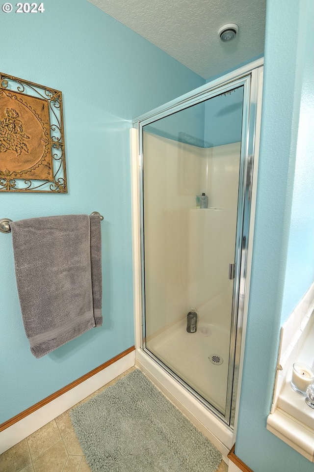 bathroom featuring a shower with door, tile patterned flooring, and a textured ceiling