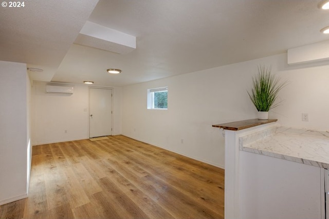 basement featuring light hardwood / wood-style flooring and an AC wall unit